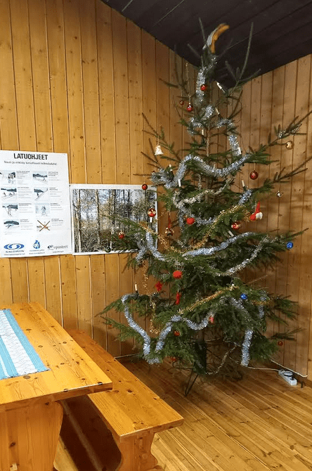 Koristeltu joulukuusu puuseinäisen tuvan nurkassa.