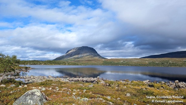 Tunturi horisontissa. Valoisa syyspäuvä vaikka pilviä taivaalla, etualalla kivikkoista maastoa ja vettä